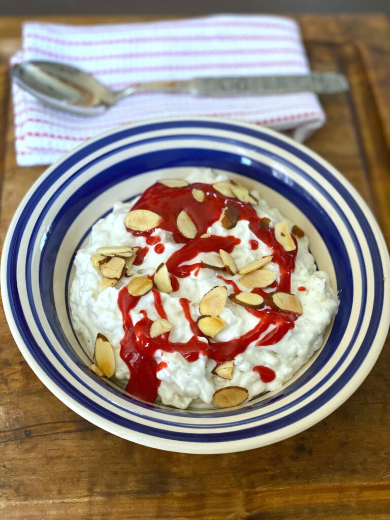 a bowl of Norwegian rice desert, riskrem, topped with sliced almonds and berry coulis