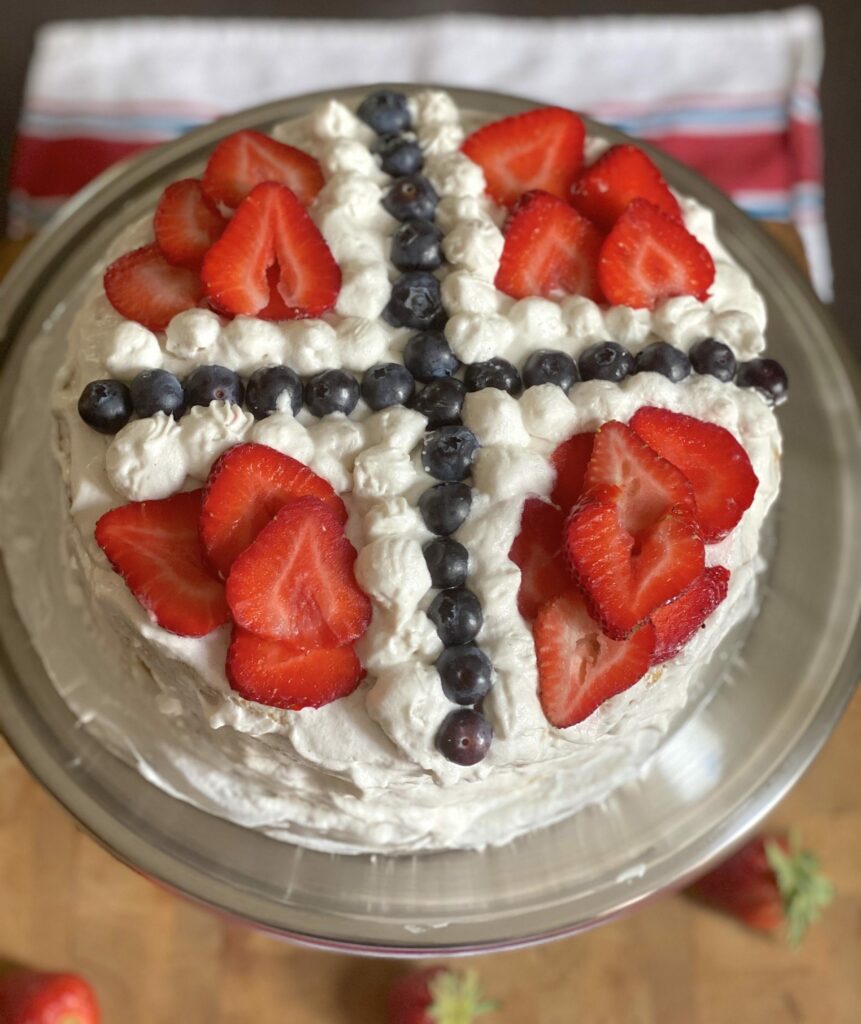 a vanilla sponge cake with vegan whipped cream frosting divided into quadrants with two lines of blueberries and sliced strawberries layered into the quadrants